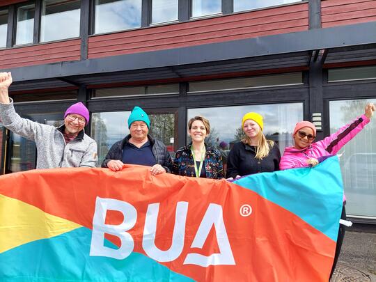 Fem blide folk holder opp BUA-banner
