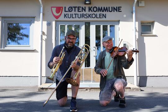 mann med trompet og trombone og mann med fiolin foran skolebygg